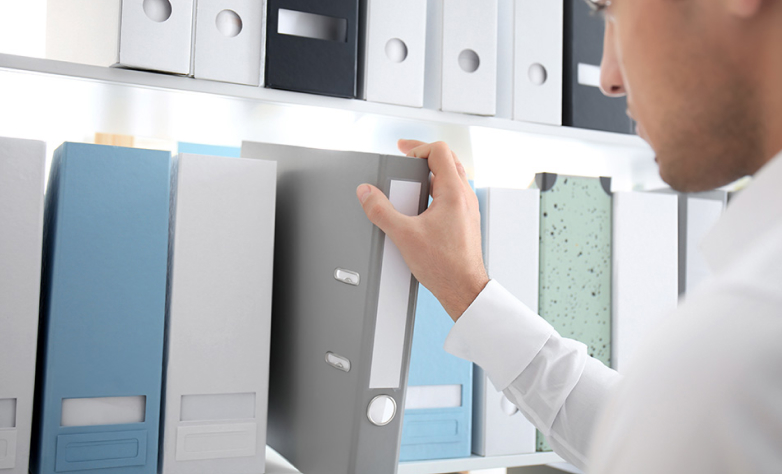 Young man taking folder with documents from shelf in archive 1